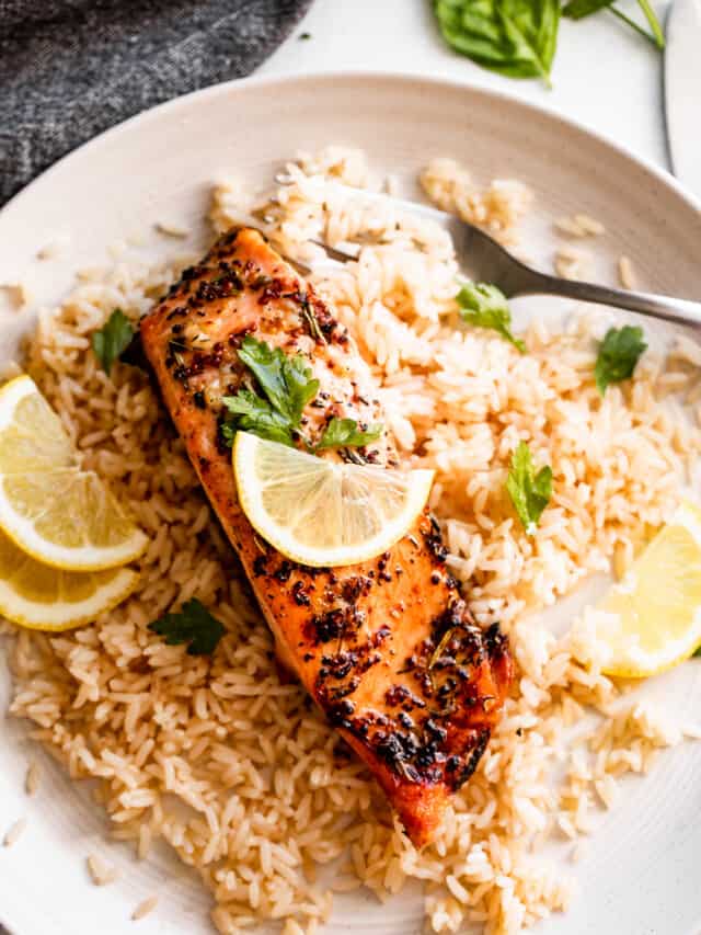 air fryer salmon fillet set atop a bed of rice and topped with lemon slices.