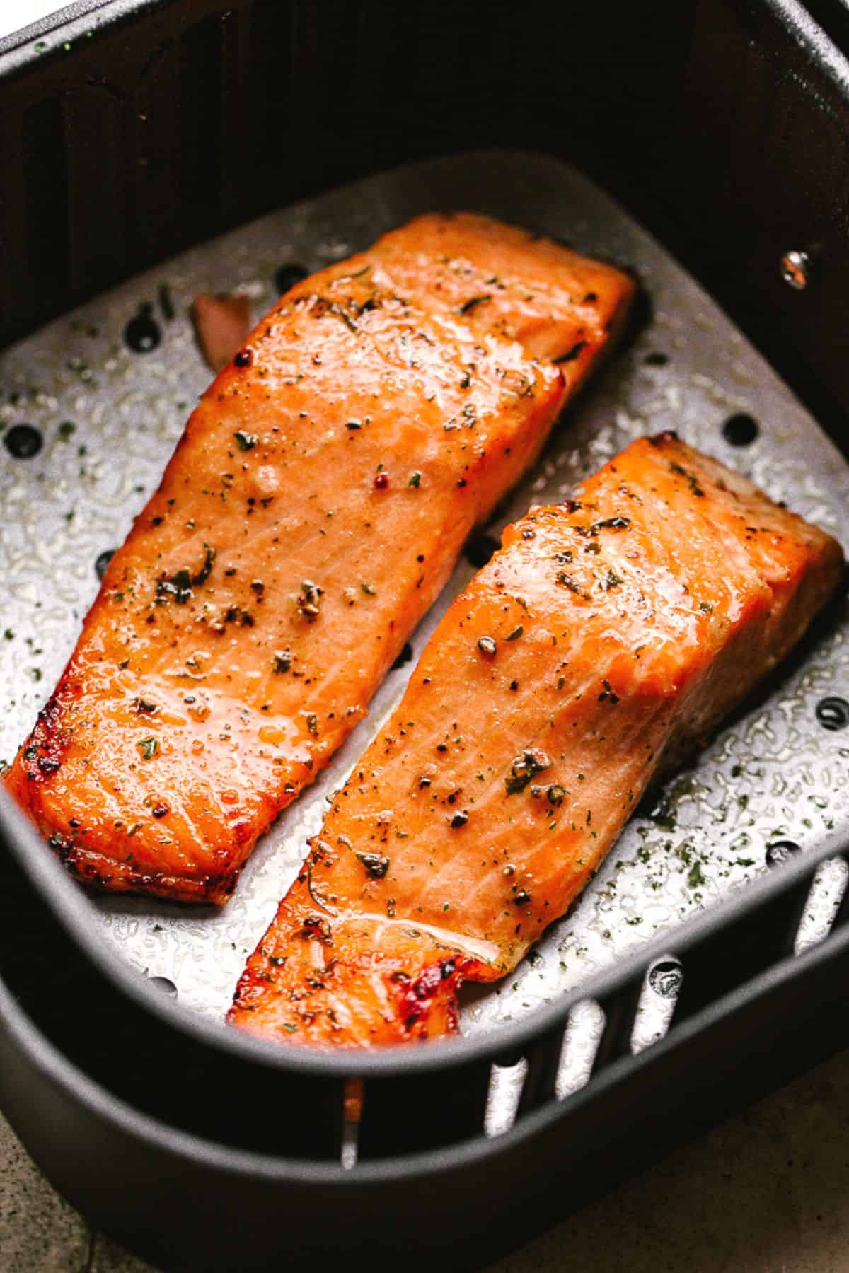 Two cooked salmon fillets in a black air fryer basket.