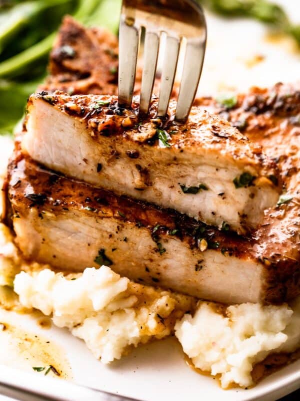 fork stabbing through a halved pork chop set on a bed of mashed potatoes