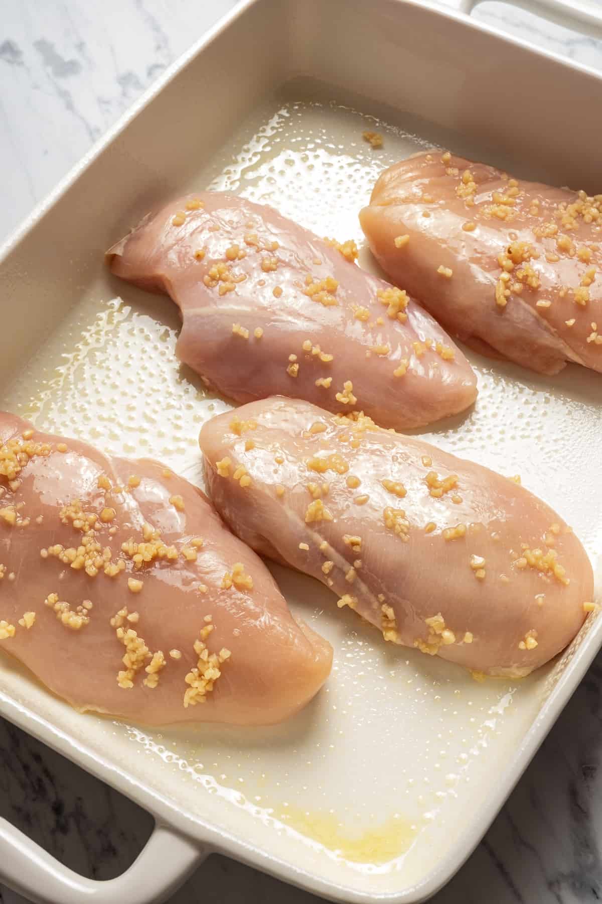 Chicken breasts in baking dish, topped with fresh garlic