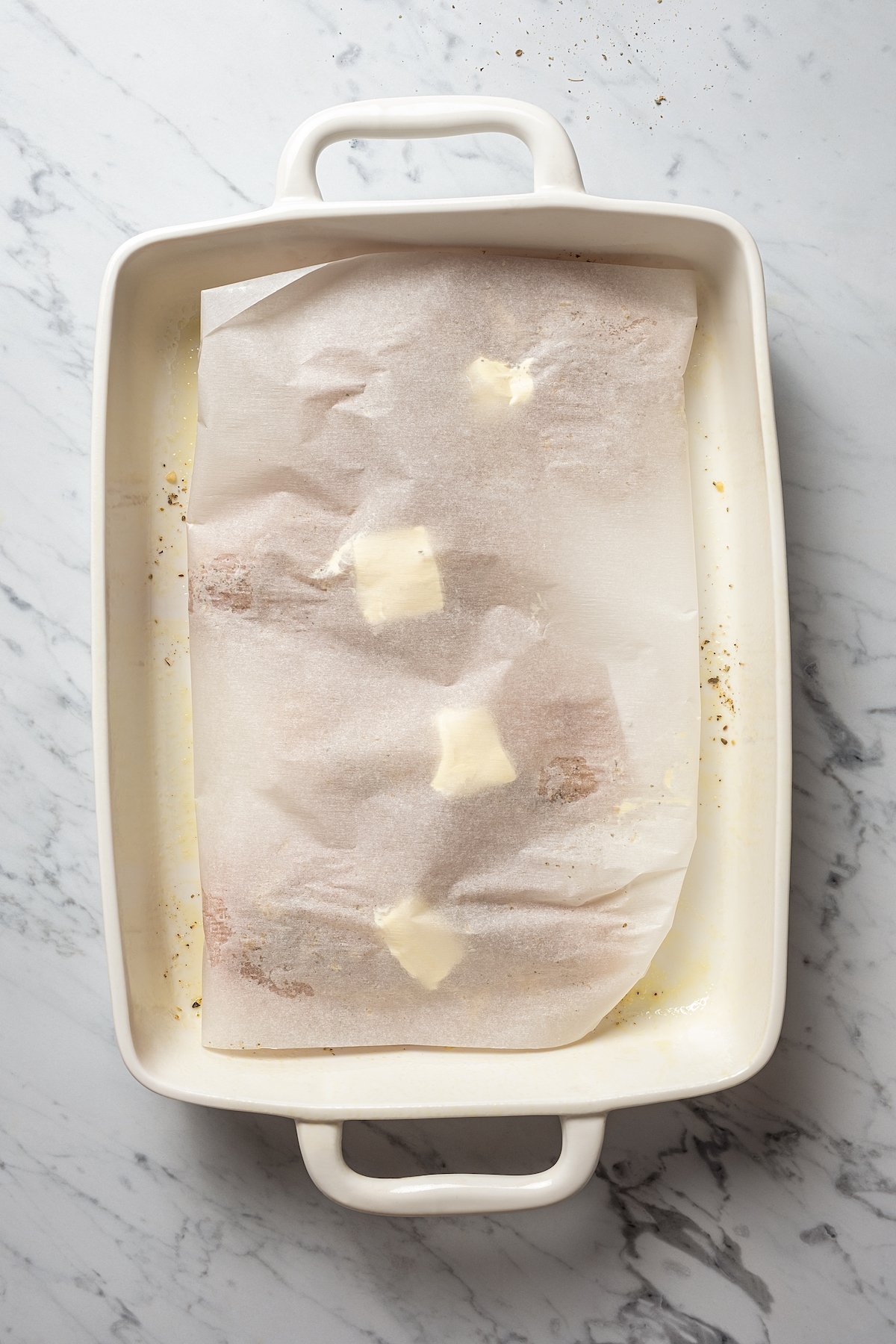 Chicken breasts in baking dish with butter and parchment paper