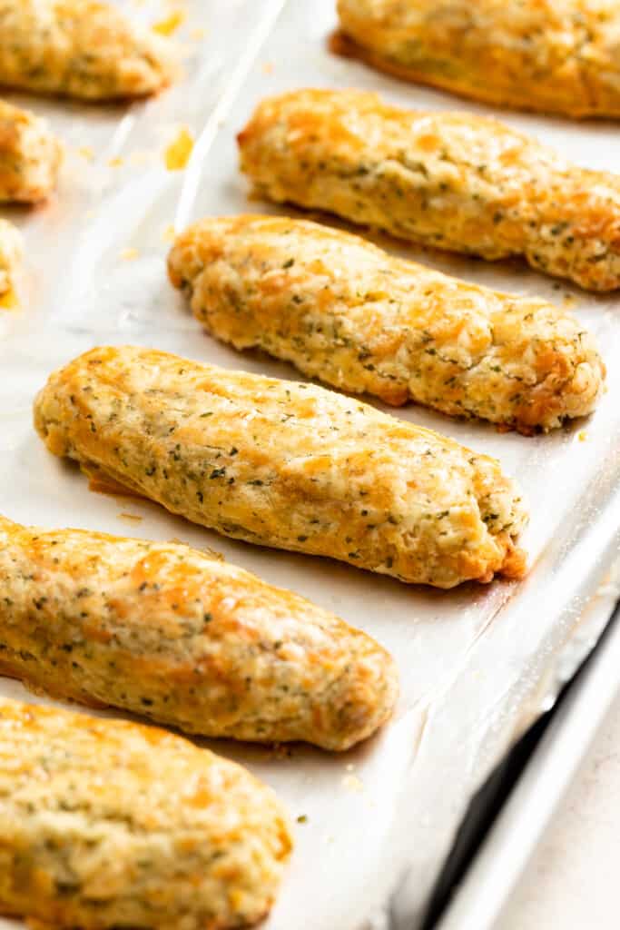 Baked mozzarella sticks arranged on a baking sheet lined with aluminum foil.