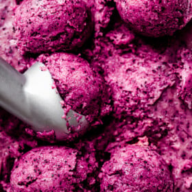 Close up of an ice cream scoop portioning balls of vegan blueberry ice cream from a loaf pan.