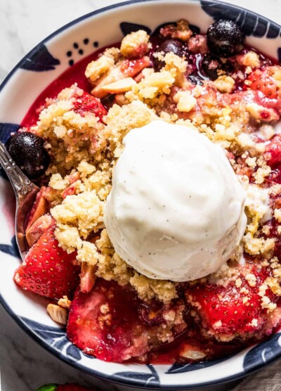 Overhead close-up shot of a bowl with blueberry strawberry crumble, and a scoop of vanilla ice cream on top.