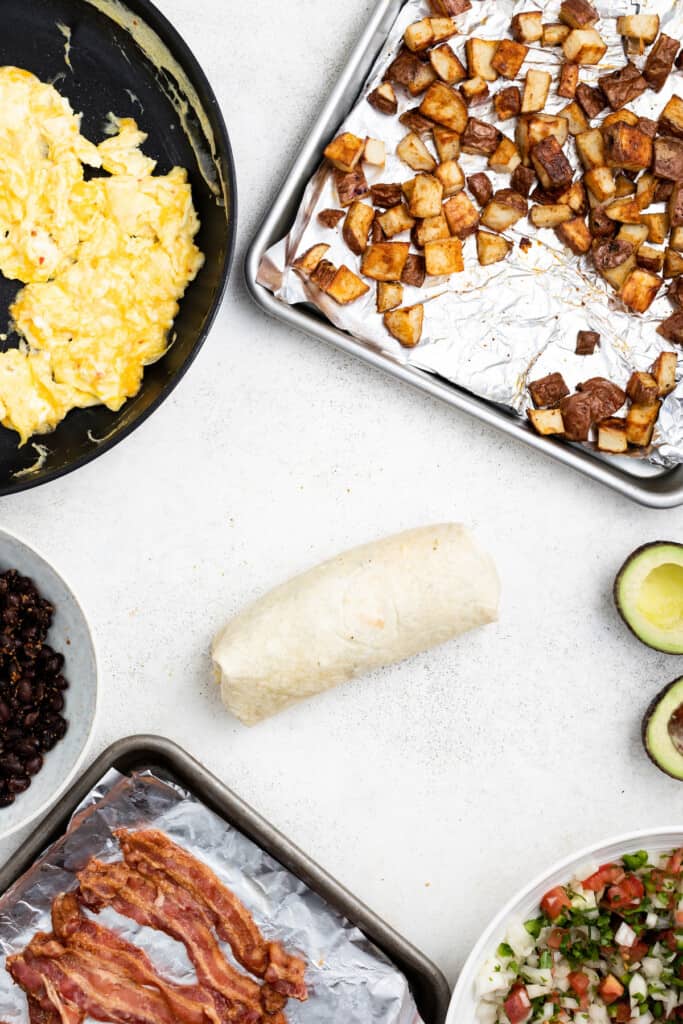 A breakfast burrito rolled neatly and surrounded by filling ingredients.