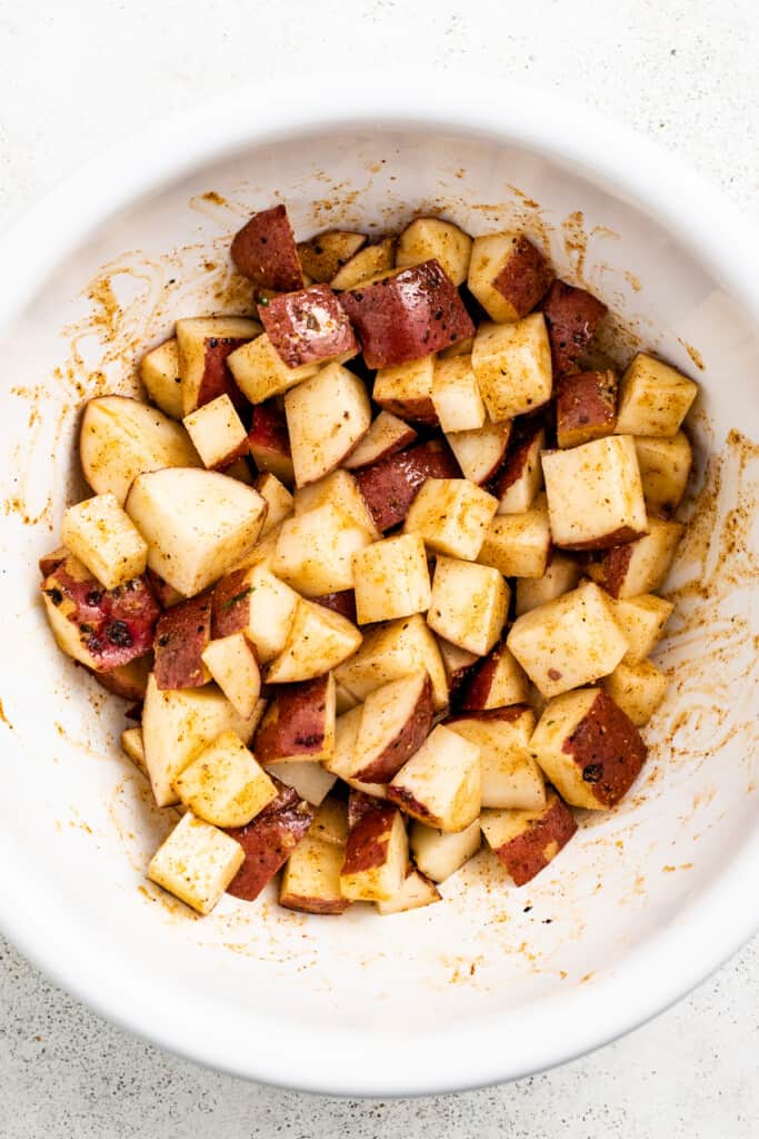 Tossing cubed potatoes in olive oil and seasoning in a mixing bowl.