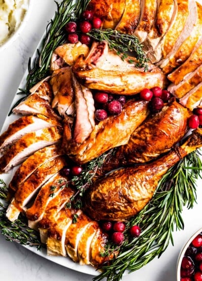 overhead shot of Sliced roasted turkey on a serving platter, surrounded with herbs and cranberries.