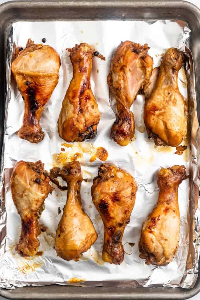 Overhead of broiled chicken adobo drumsticks on a sheet pan.