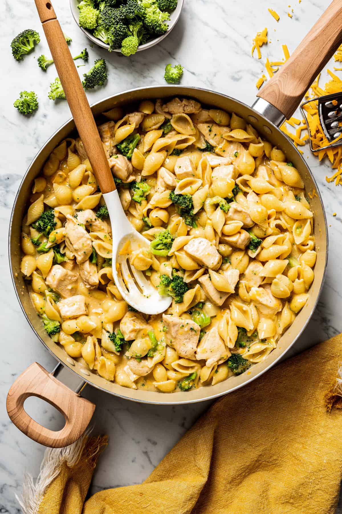A large skillet full of chicken and broccoli pasta with a slotted spoon.