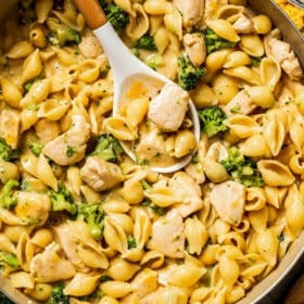 Close up overhead photo of a large skillet full of chicken and broccoli pasta with a slotted spoon.