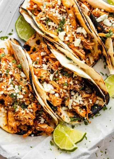 four chicken tinga tacos arranged on a plate and topped with cheese