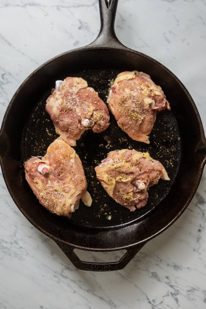 Browning chicken thighs, skin-side down in a pan.