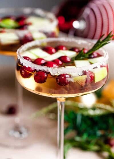 up close shot of two coupe glasses filled with prosecco and garnished with fresh cranberries, apples, and rosemary sprigs