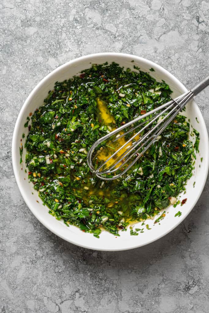 Whisking chimichurri in a bowl.