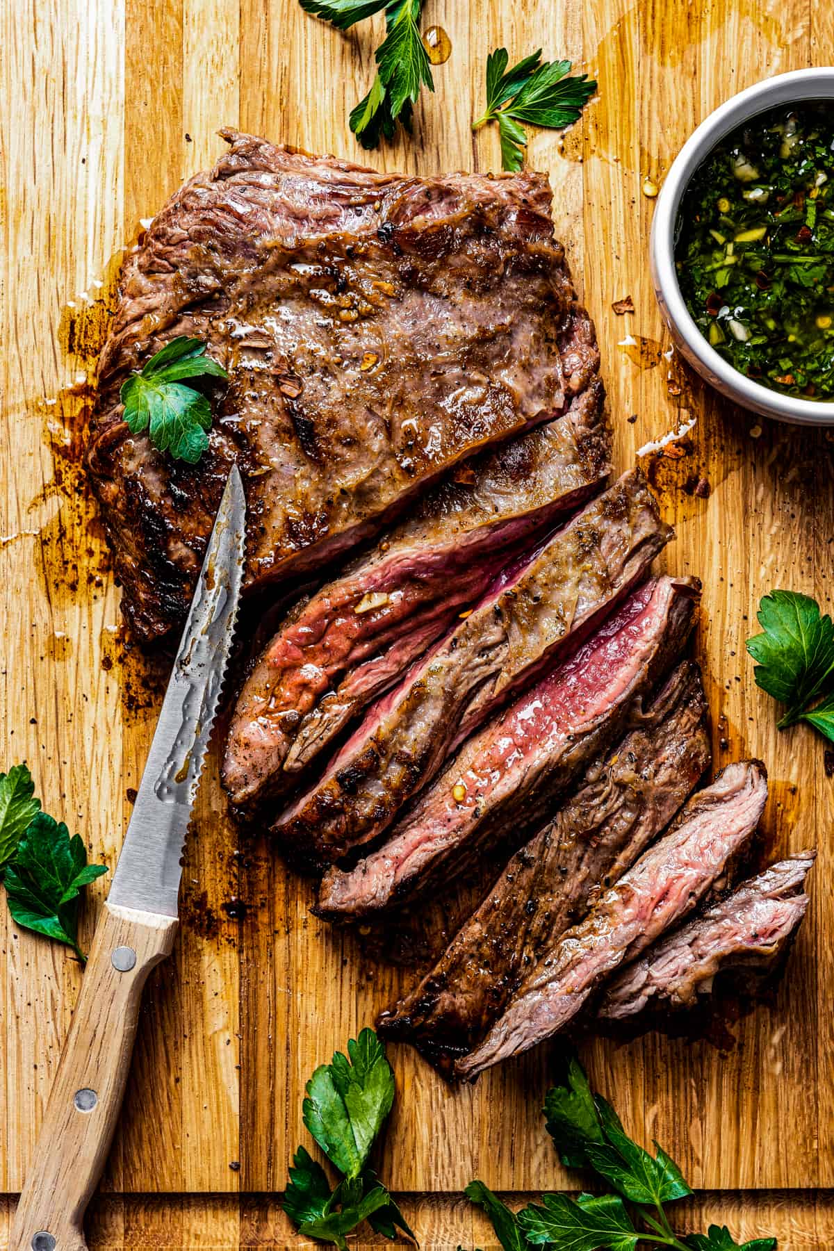 Churrasco steak on a cutting board with a knife and a bowl of chimichurri.