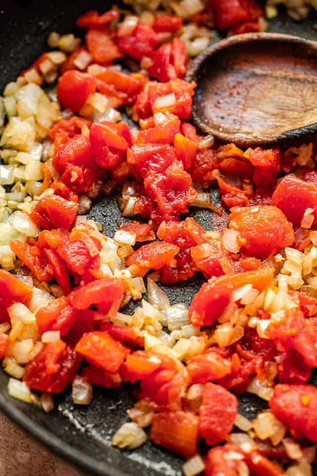 frying onions and diced tomatoes in a black skillet