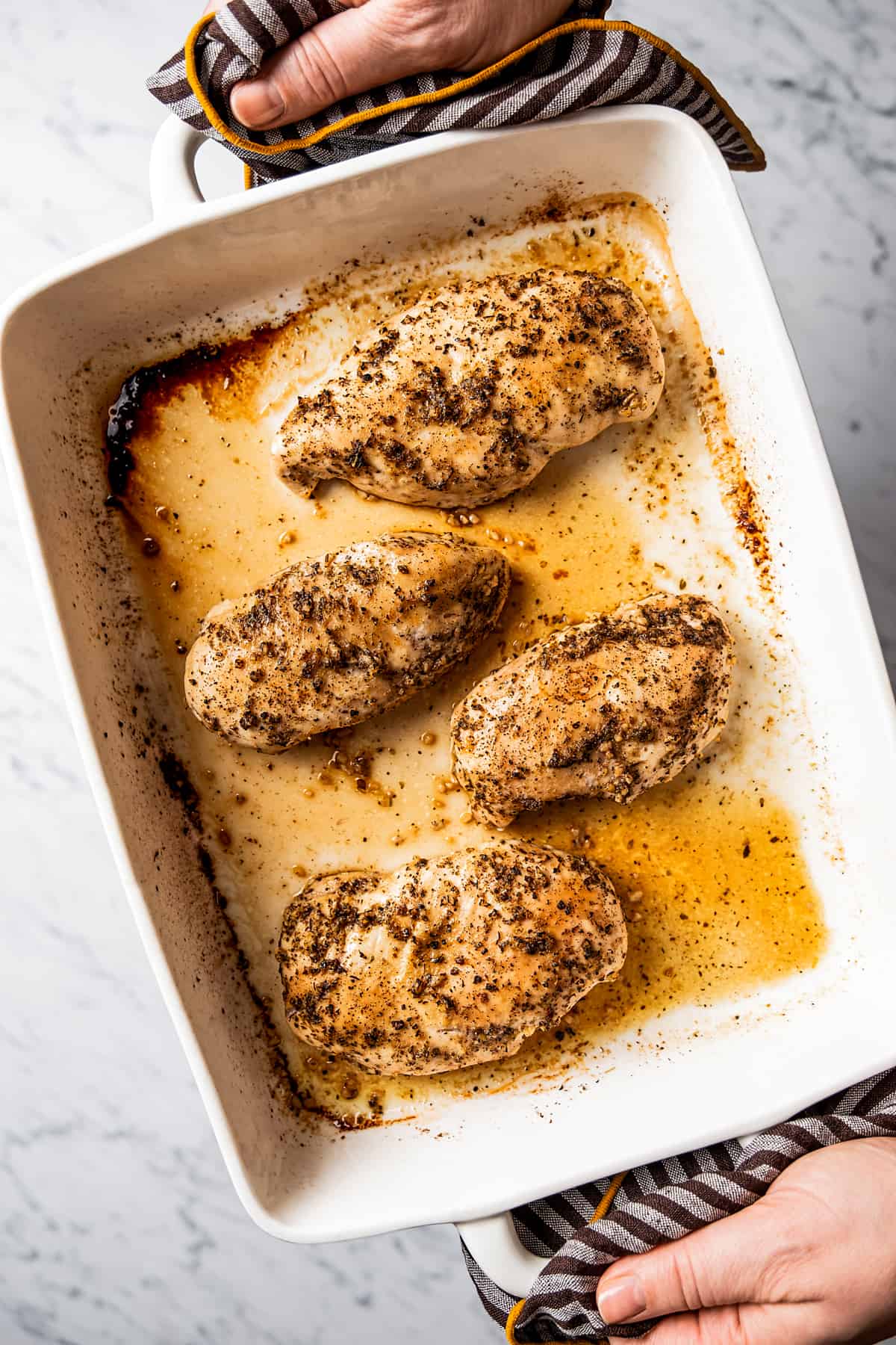 Hands holding baked chicken breasts in baking dish