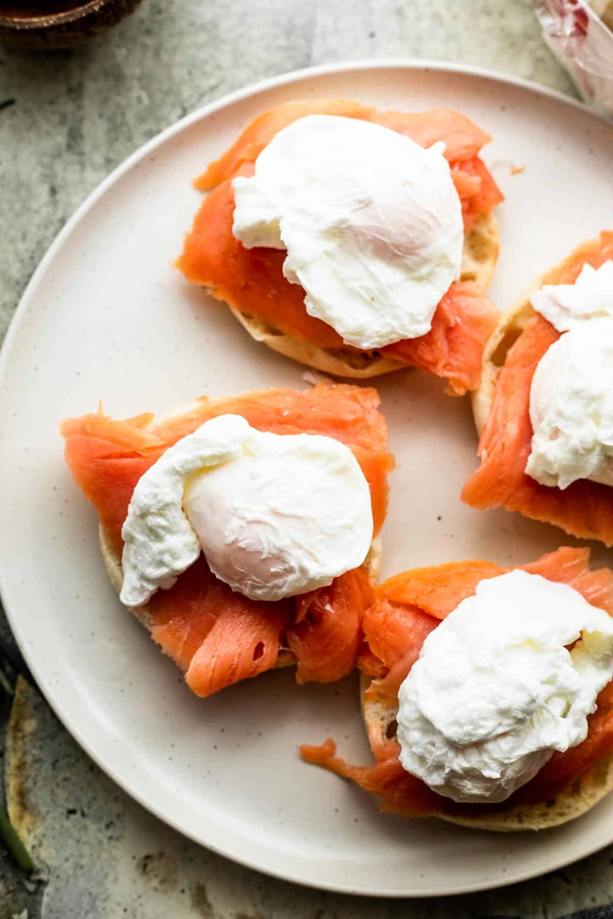 overhead shot of four english muffins topped with slices of smoked salmon and poached eggs on top.