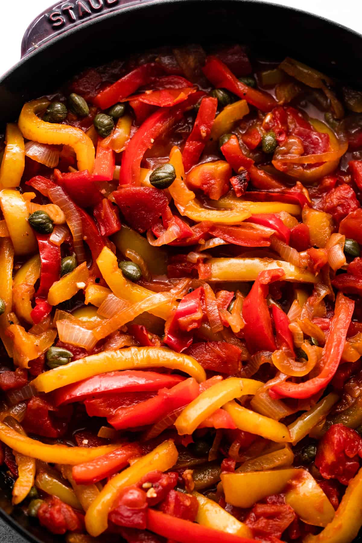overhead shot of a skillet with sliced yellow and red peppers cooking in it.