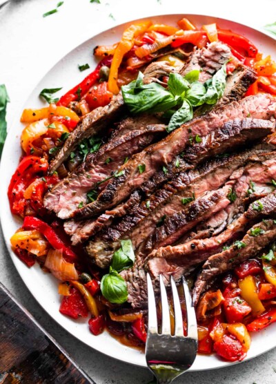 slices of grilled flank steak served over a bed of peperonata, with a large serving fork placed at the bottom of the plate.