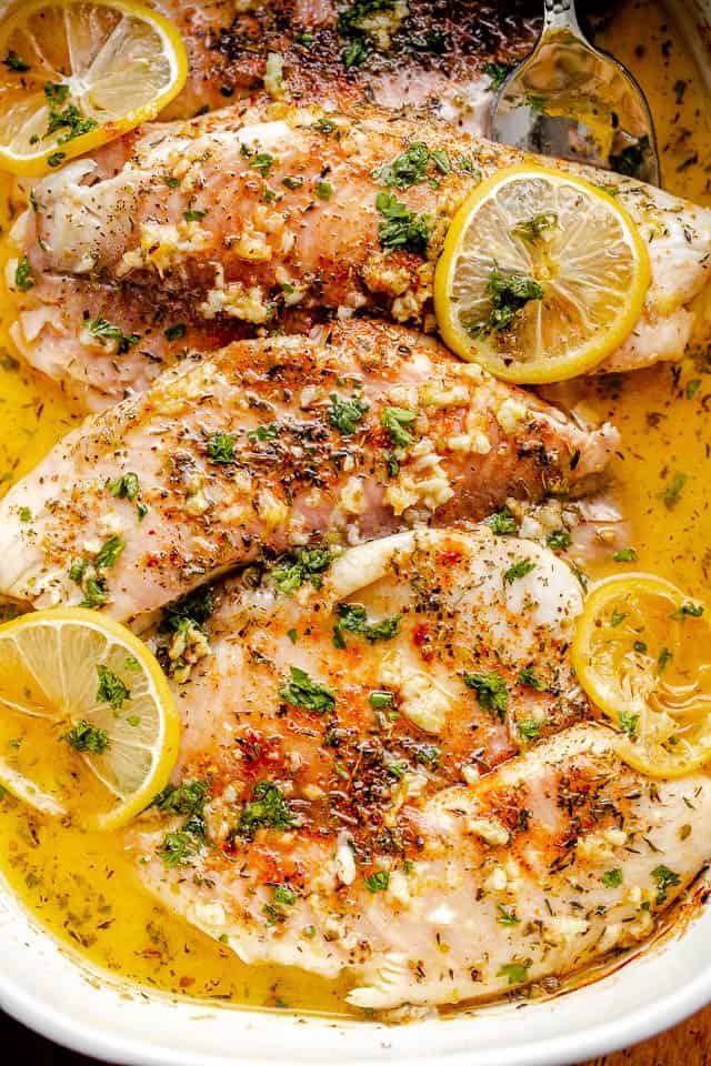 overhead shot of baked tilapia in baking dish topped with garlic and lemon slices