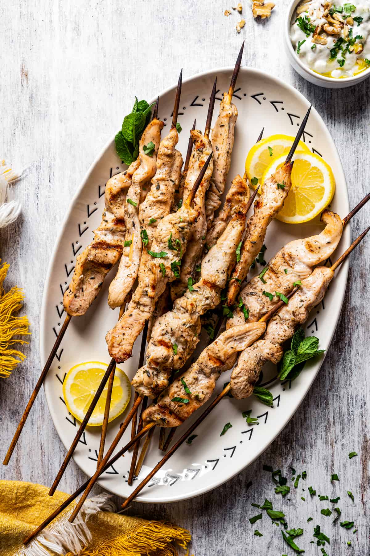 A serving plate with cooked chicken skewers and lemon wedges.