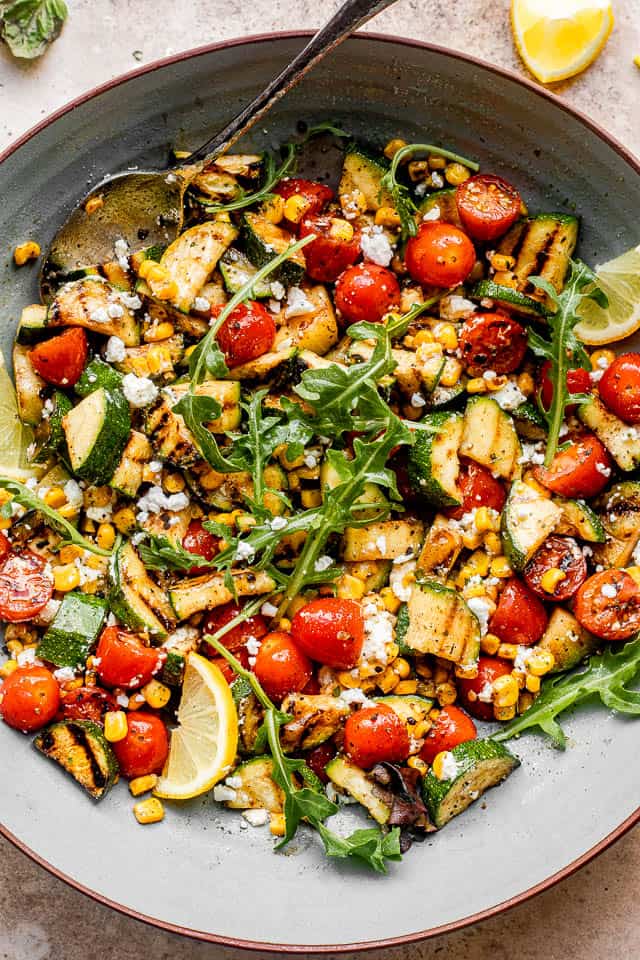 top view of a large blue salad bowl filled with grilled zucchini slices, cherry tomatoes, and corn kernels