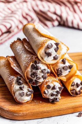 Six cannolis forming a pyramid on a cutting board with a kitchen towel in the background.