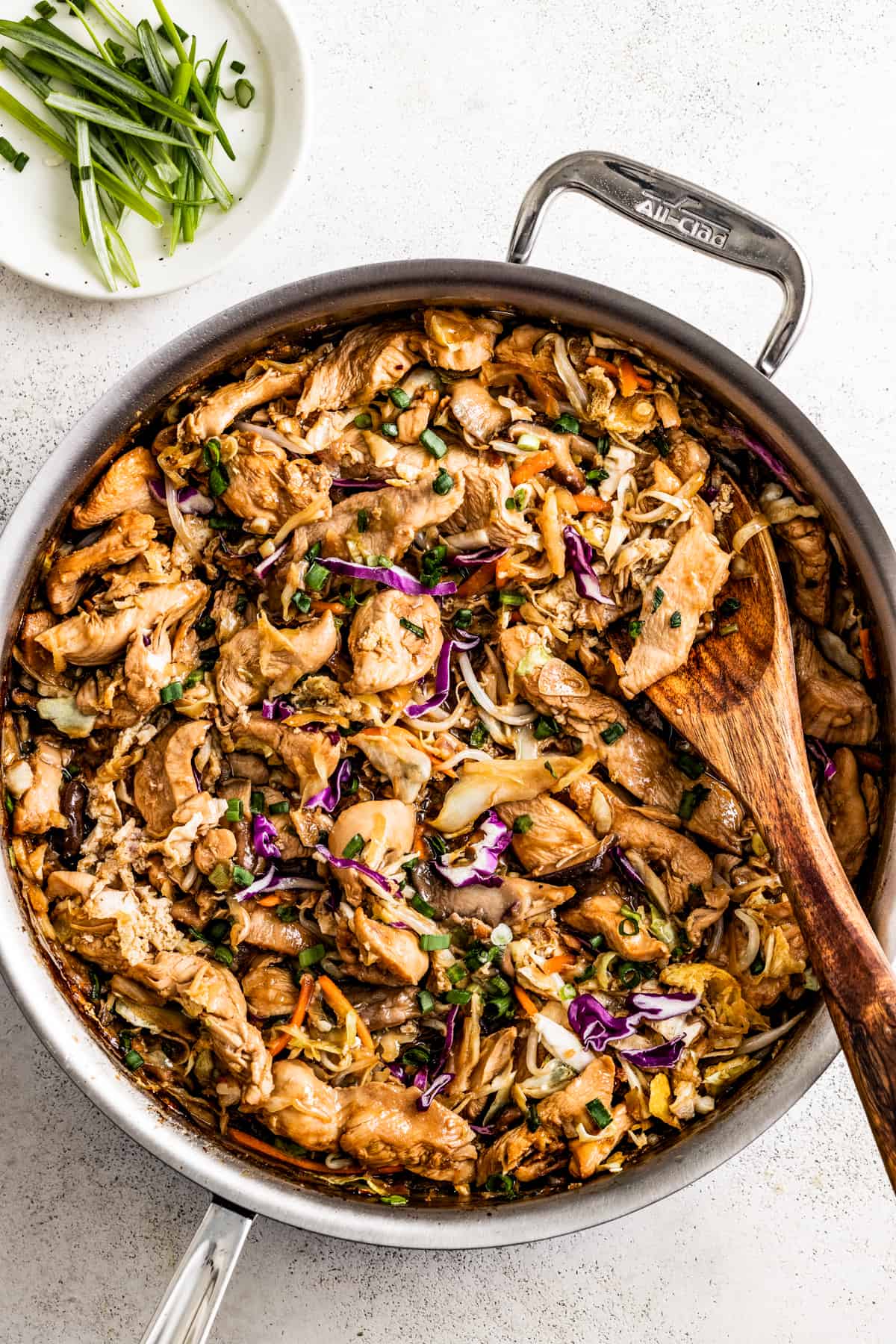 overhead shot of moo shu chicken in a skillet, with a wooden spoon stirring through it.