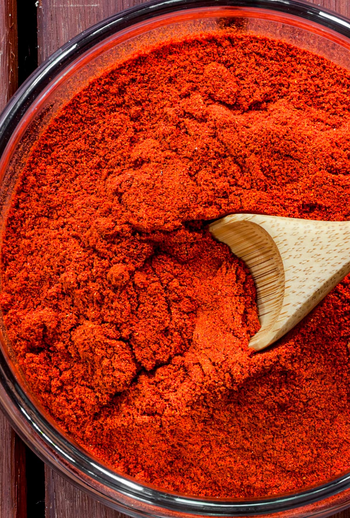 Up close photo of ground paprika in a glass bowl, with a wooden spoon stirring through it.