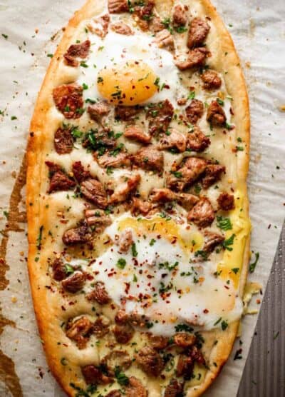 overhead shot of Pastrmajlija pizza topped with chunks of pork and fried eggs.