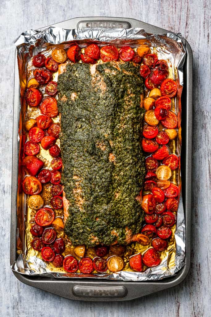 Baked salmon with pesto and tomatoes on a sheet pan.