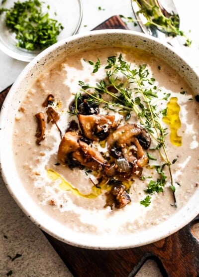 overhead photo of creamy mushroom soup and rice in a bowl garnished with whole mushrooms, greens, and a swirl of heavy cream.