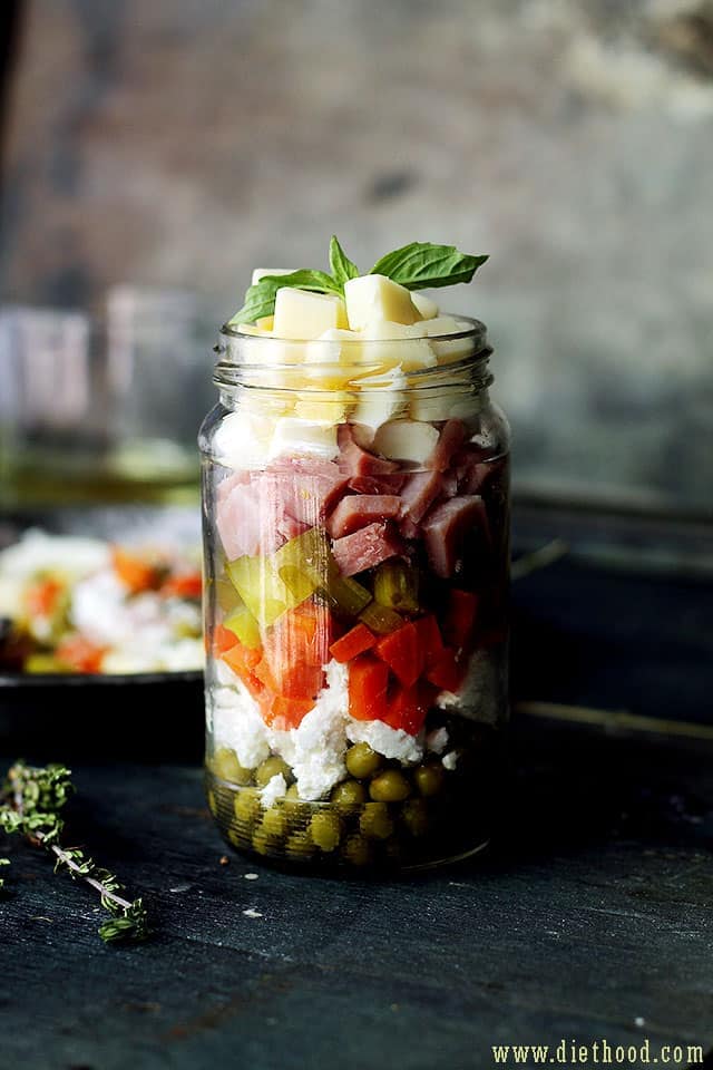 Russian Layered Salad in a jar with stacked up ham, eggs, cheeses, carrots, peas, and pickles. | 
