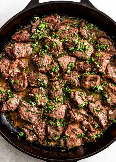 Garlic butter steak bites in a cast iron skillet, and they're garnished with parsley.