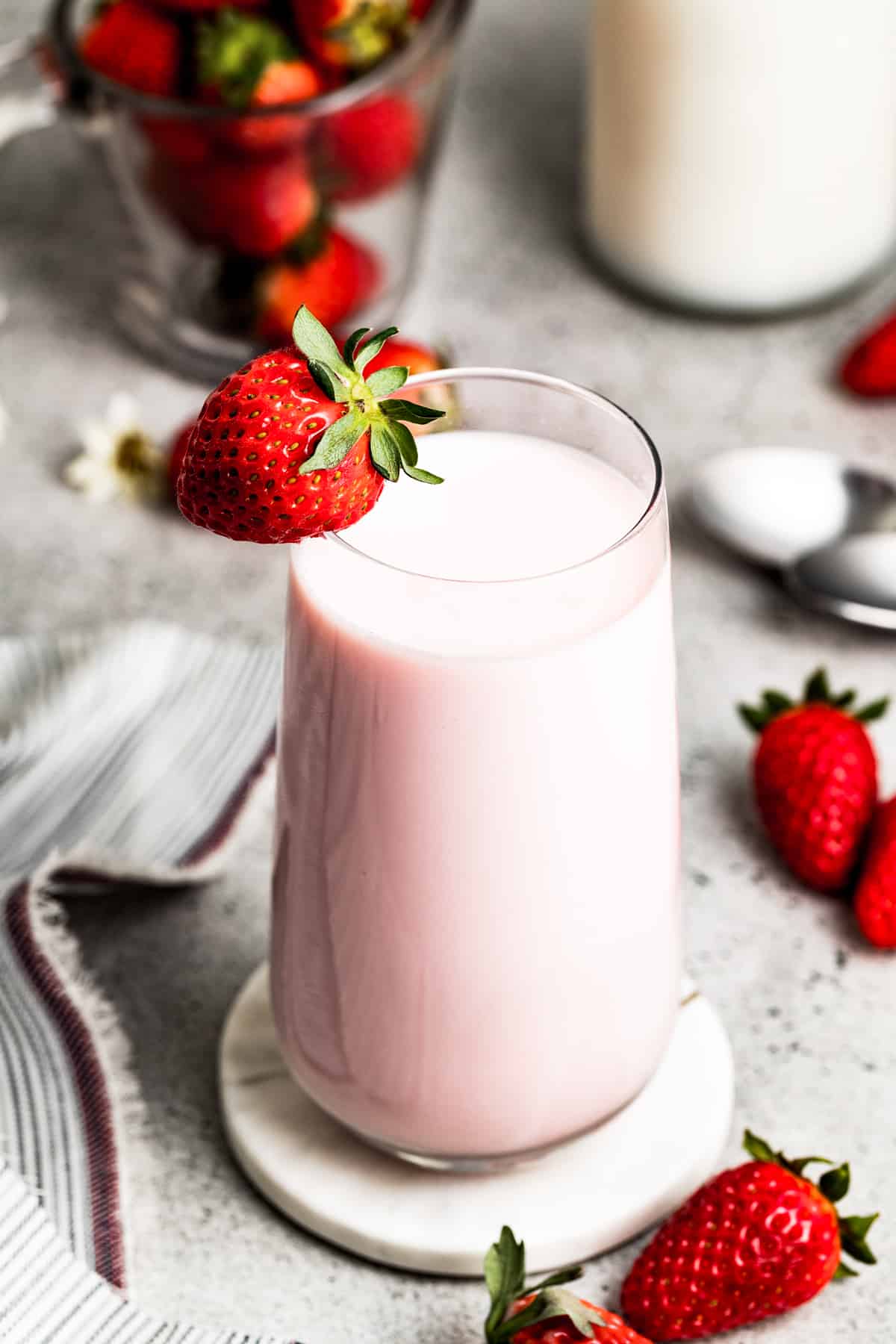 Strawberry milk in a glass with a strawberry on the edge of the glass, and fresh strawberries arranged around the glass of milk.