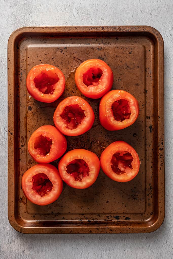 Overhead view of eight hollowed out tomatoes arranged on a metal baking sheet.