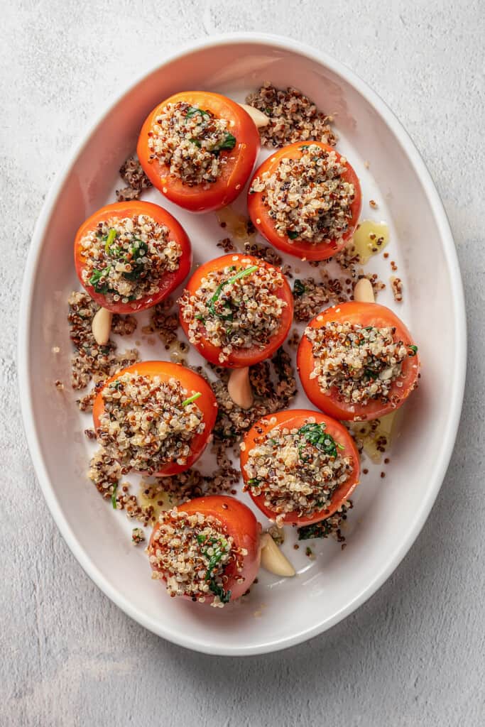 Overhead view of tomatoes stuffed with quinoa filling in a white ceramic baking dish.