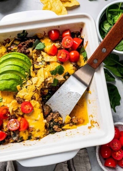Overhead view of a baked taco casserole in a square baking dish with a serving missing from the corner, with a spatula left in the pan.