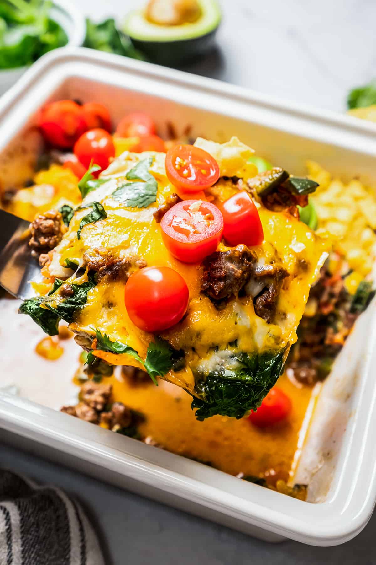 A slice of taco casserole lifted from the rest of the casserole in a square baking dish.