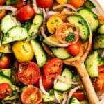 Closeup of tomato and cucumber salad in a serving bowl with a wooden spoon.