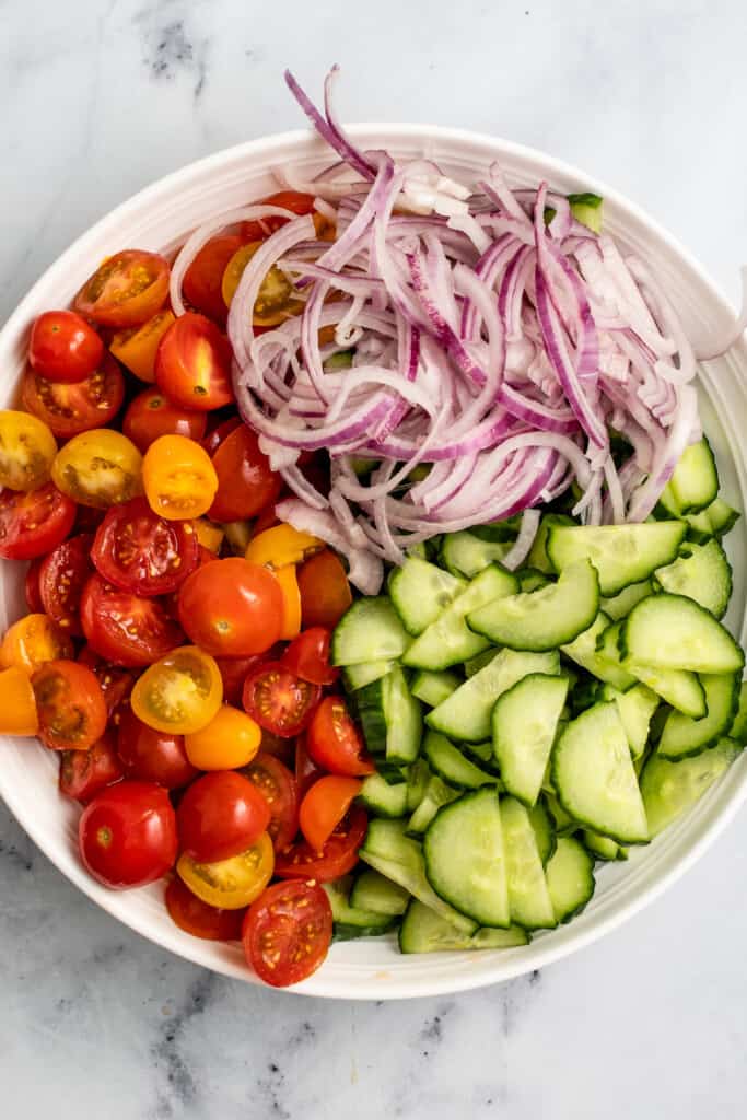 Tomato, cucumber, and red onion in a bowl before being mixed together.