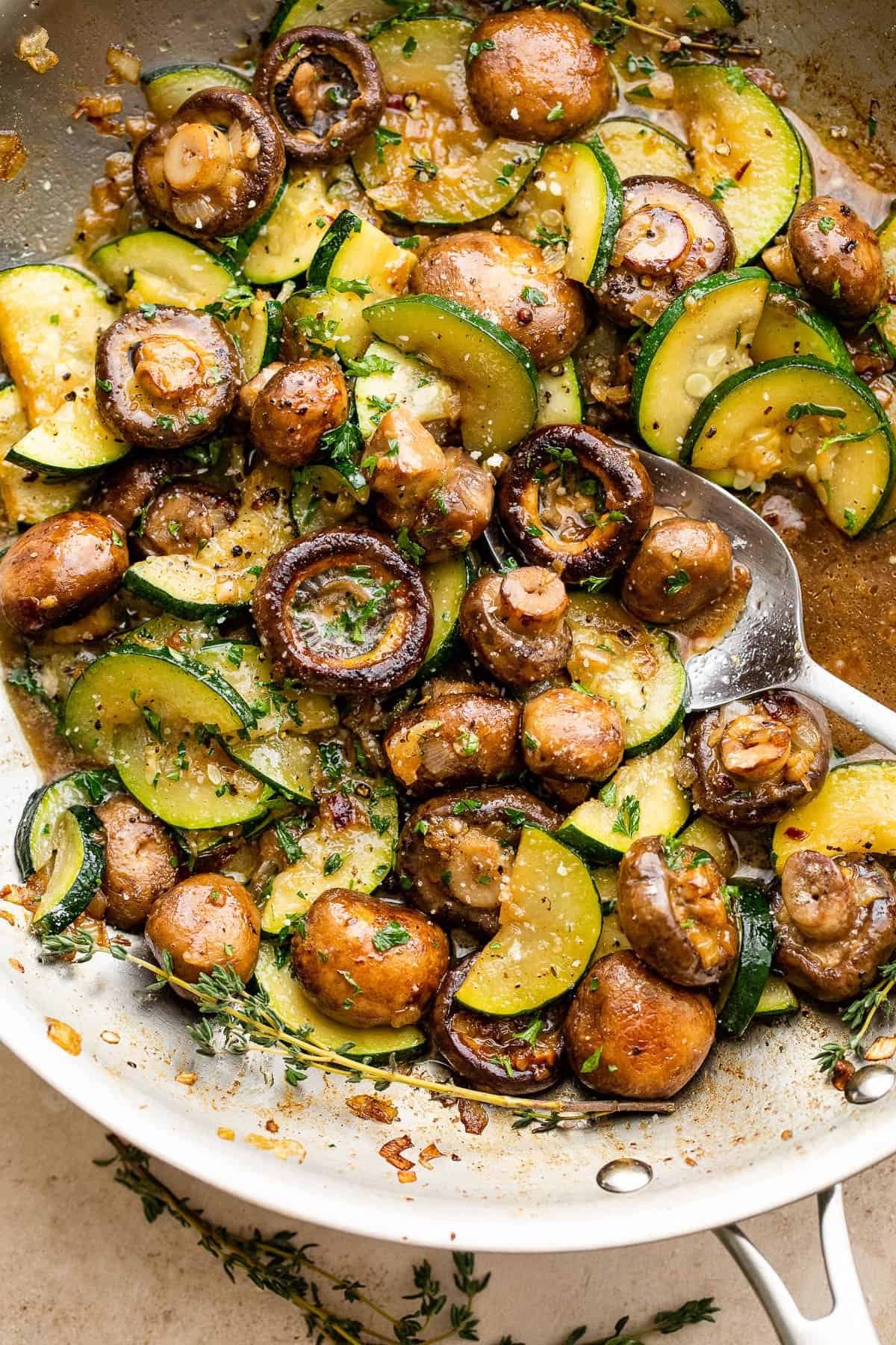 sliced zucchini and button mushrooms cooking in a stainless steel skillet